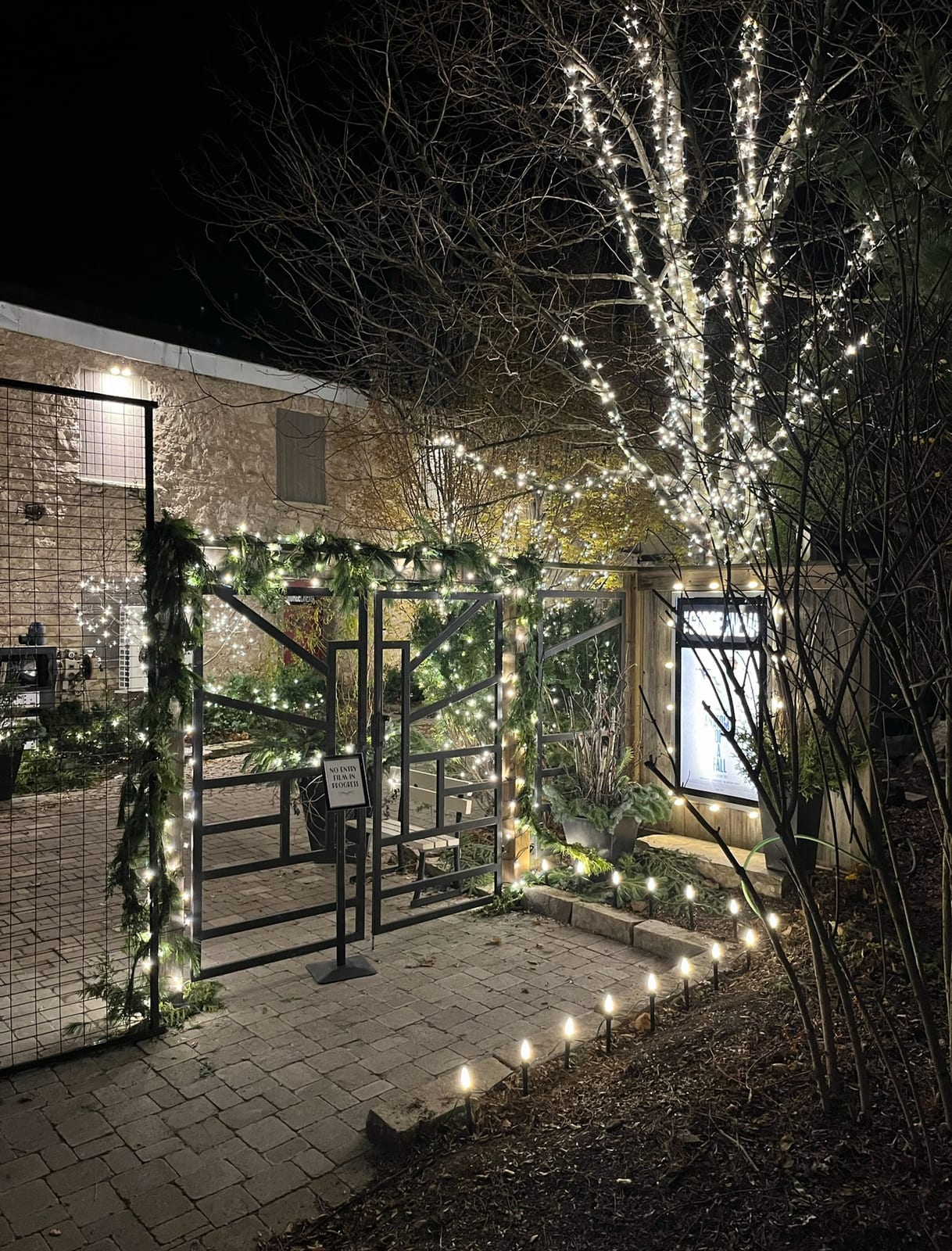 Holiday lights and garland frame a courtyard entrance beside a stone building