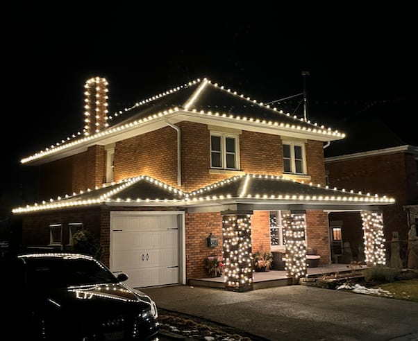 Warm-white holiday lights outlining a brick home and porch columns.