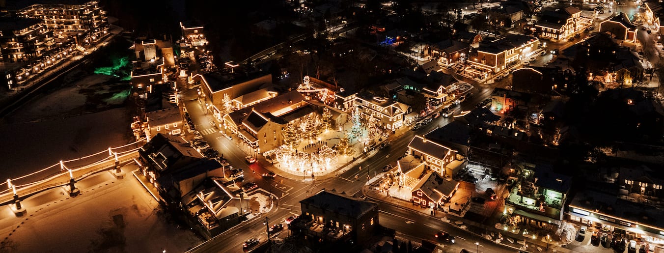 Aerial view of buildings, a bridge and trees illuminated for the holidays.