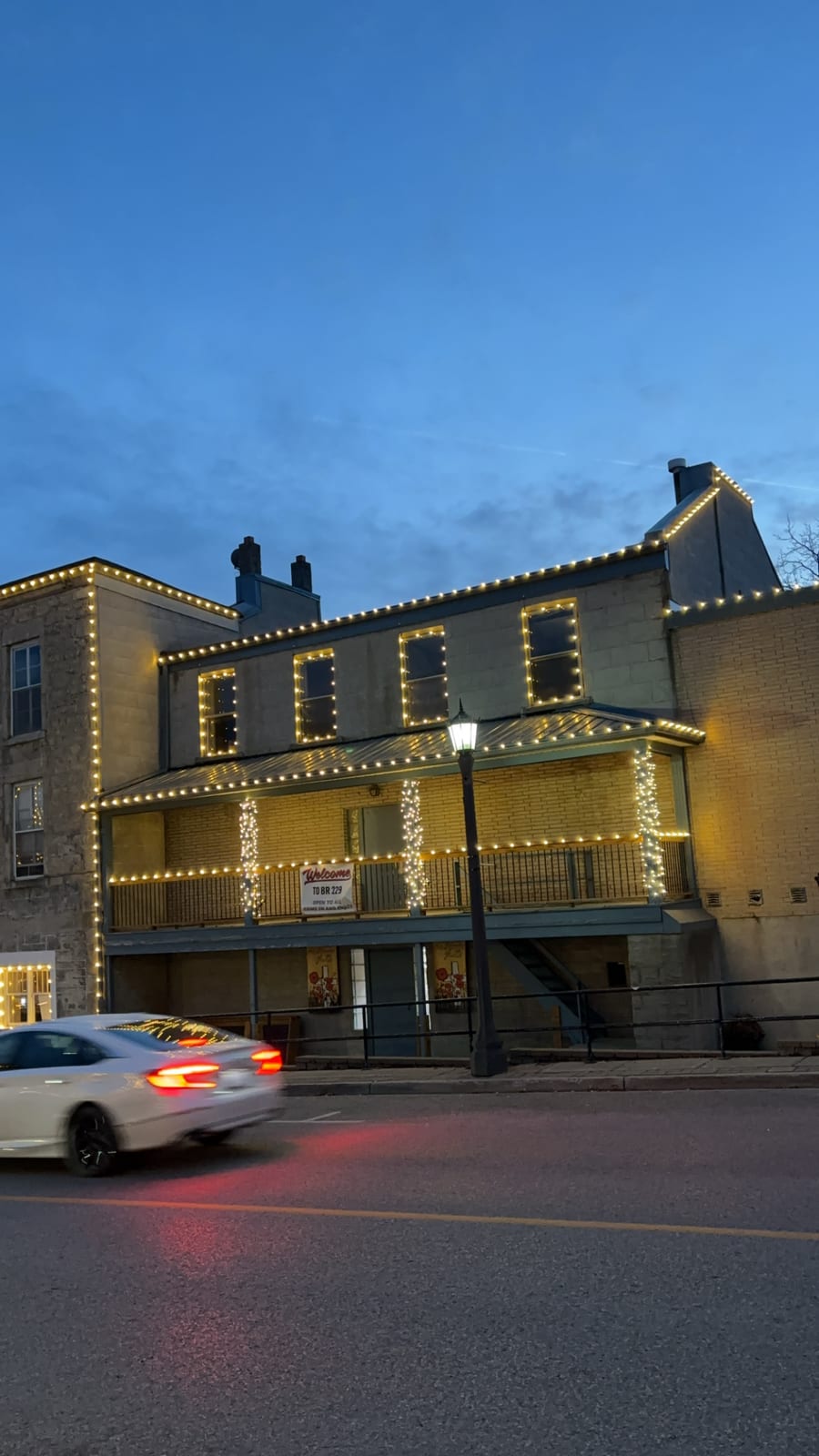 Warm-white lights outline a stone building’s roofline, windows and porch