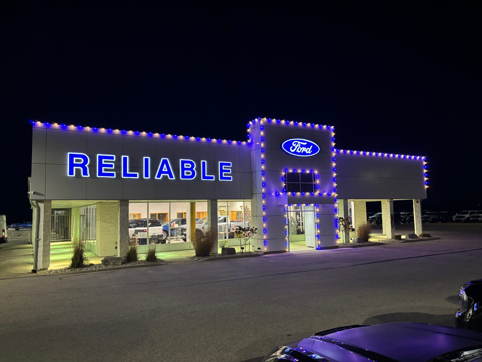 Blue and warm-white holiday lighting outlining a Reliable Ford dealership.